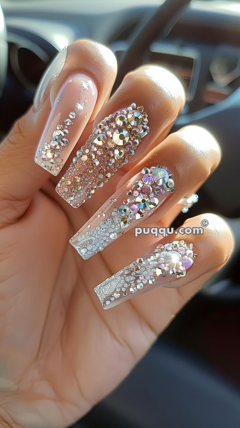 Long coffin-shaped acrylic nails adorned with various sparkling rhinestones and intricate silver designs.