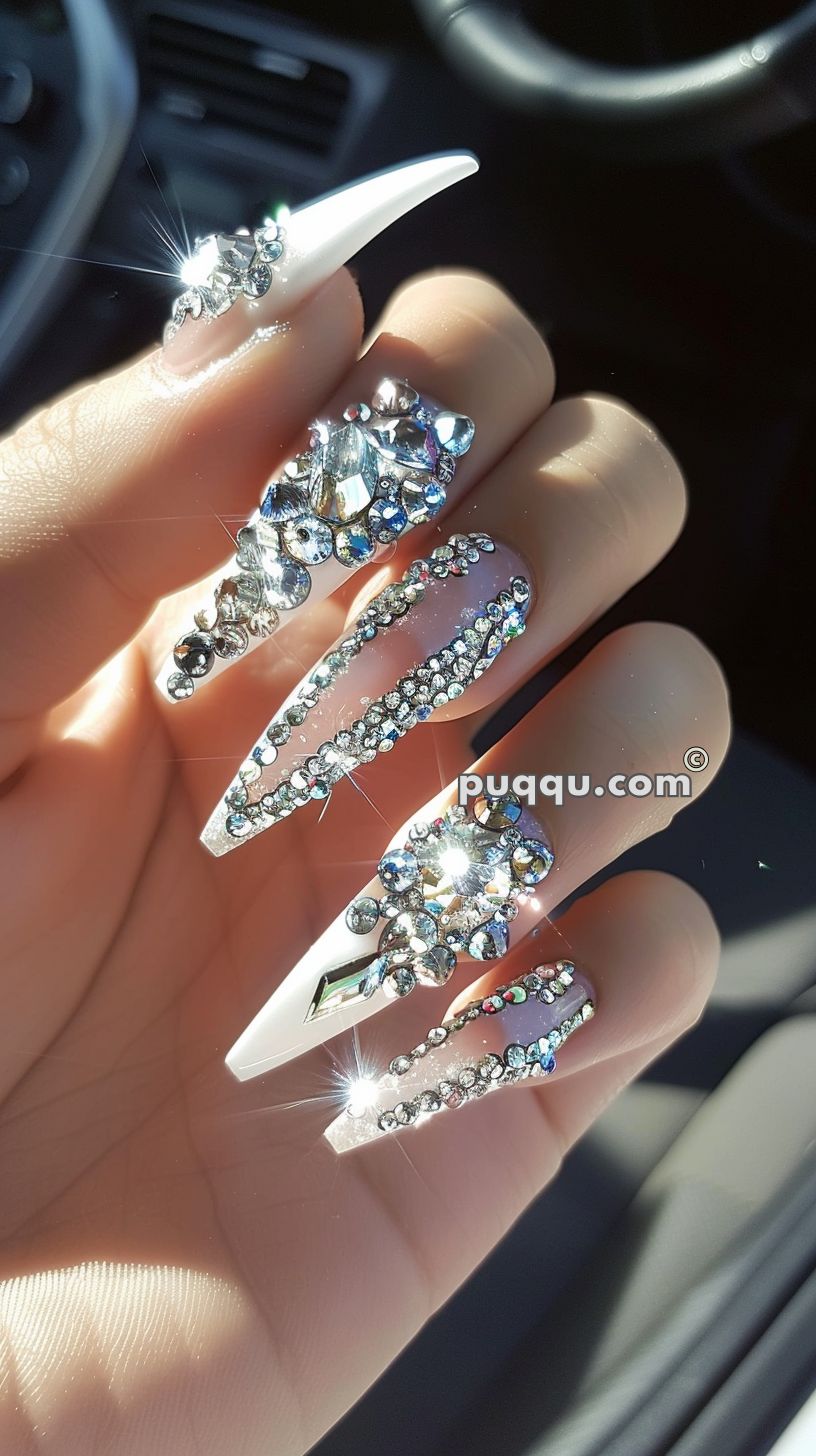 Long, pointed white nails adorned with intricate, sparkling crystal decorations and rhinestones.