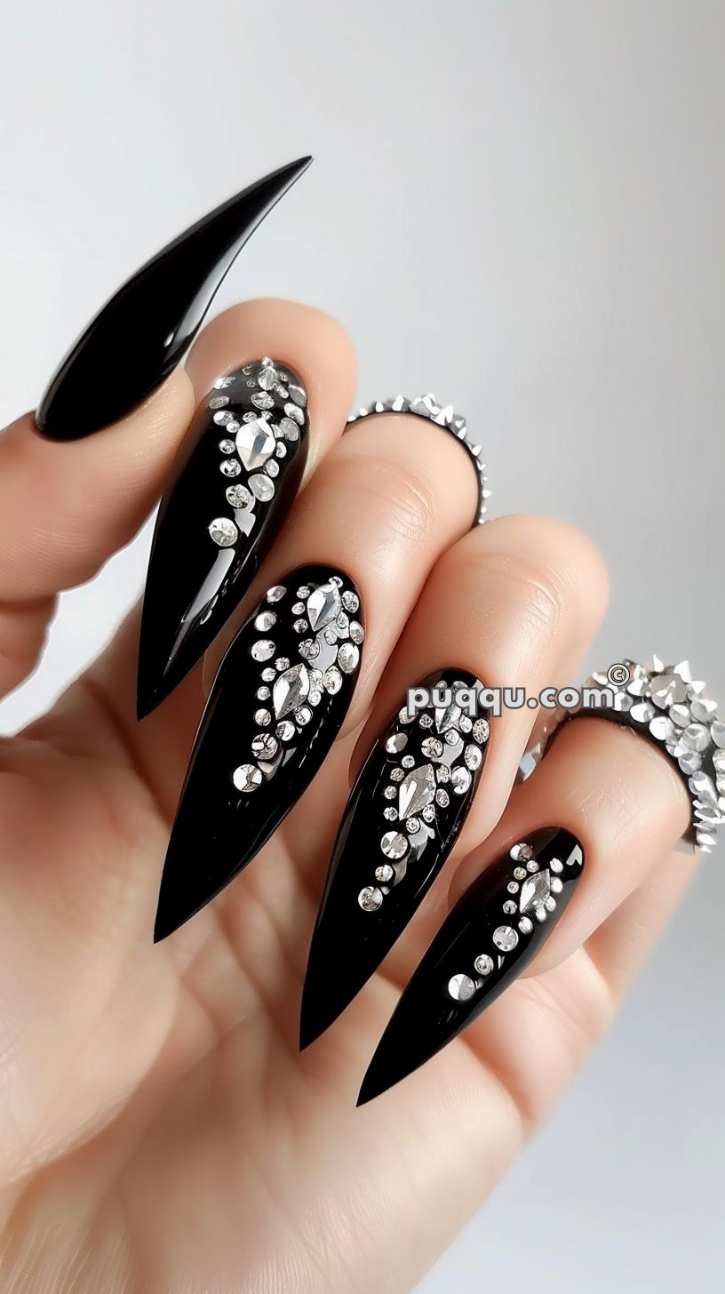 Long black stiletto nails with silver rhinestone designs.