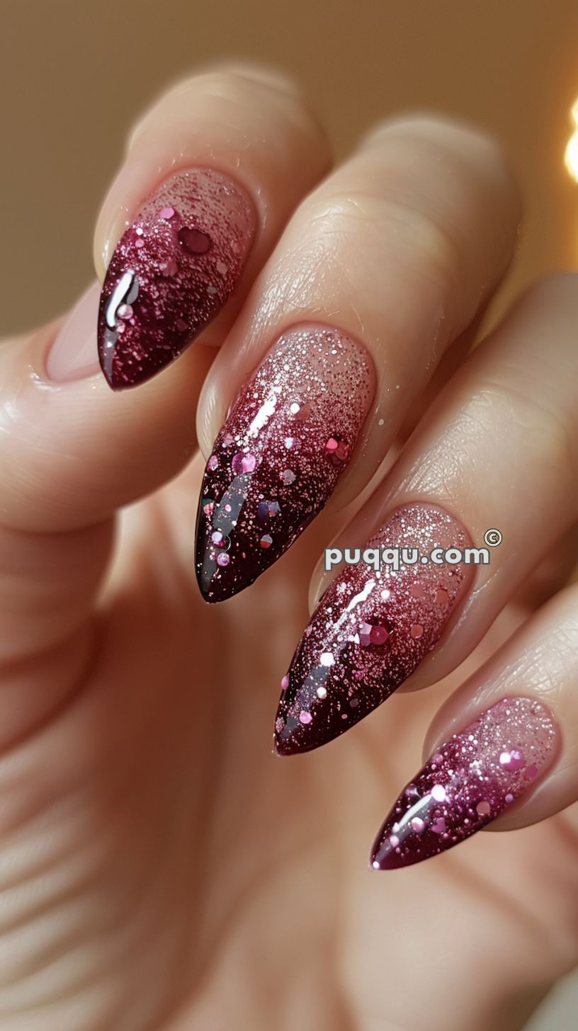 Close-up of a hand with stiletto-shaped nails painted in a pink and burgundy ombre gradient with glitter and sequin accents.