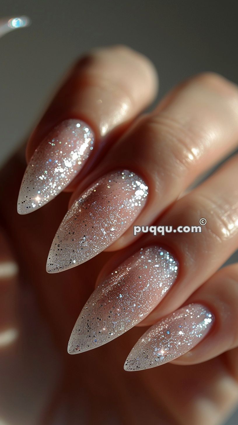 Close-up of a hand with long, pointed nails featuring a glittery, sparkling nail polish.