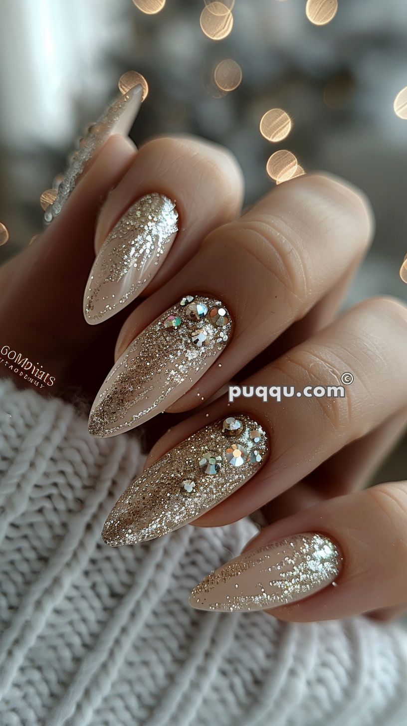 Close-up of hand with almond-shaped nails, featuring a nude base with silver glitter and rhinestone embellishments.