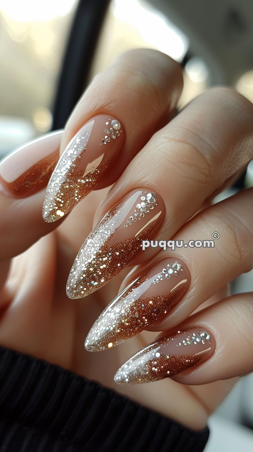 Close-up of almond-shaped nails with a golden glitter ombre effect and small rhinestone accents on each nail.