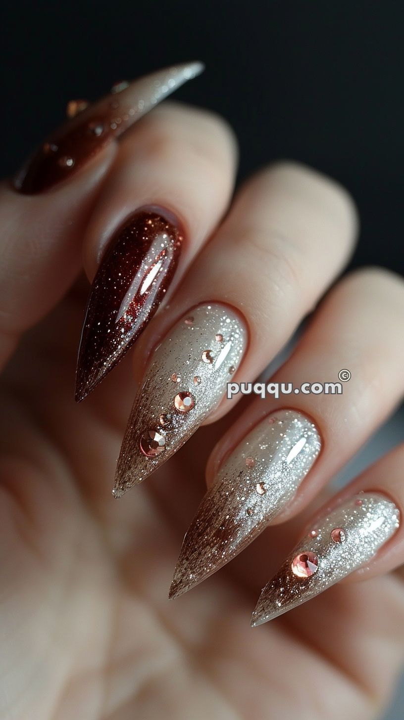 Long, pointed nails with brown and beige gradient design, adorned with shiny rhinestones and glitter.