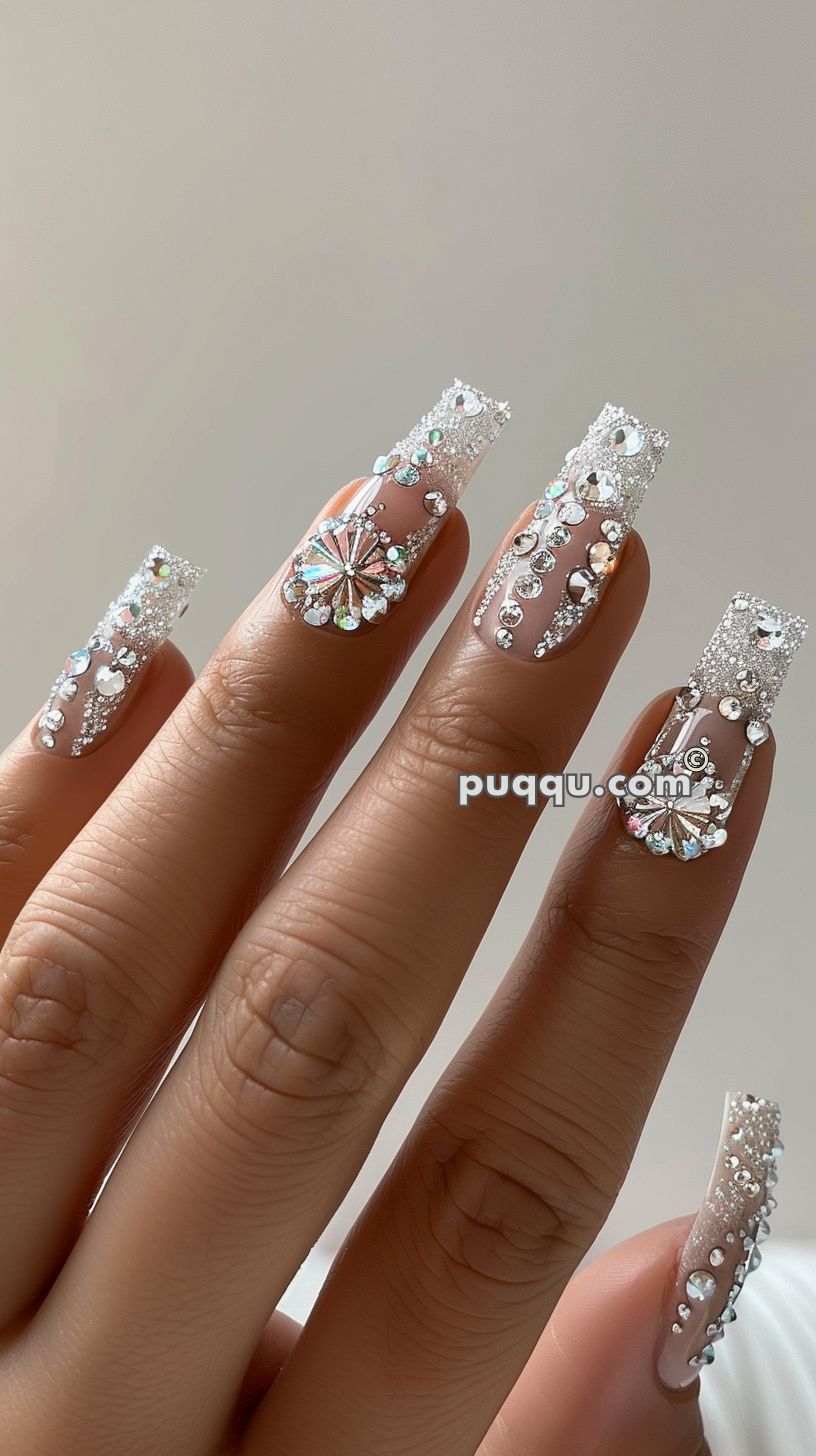 Hand with long nails featuring intricate, sparkling, silver designs, and adorned with rhinestones.