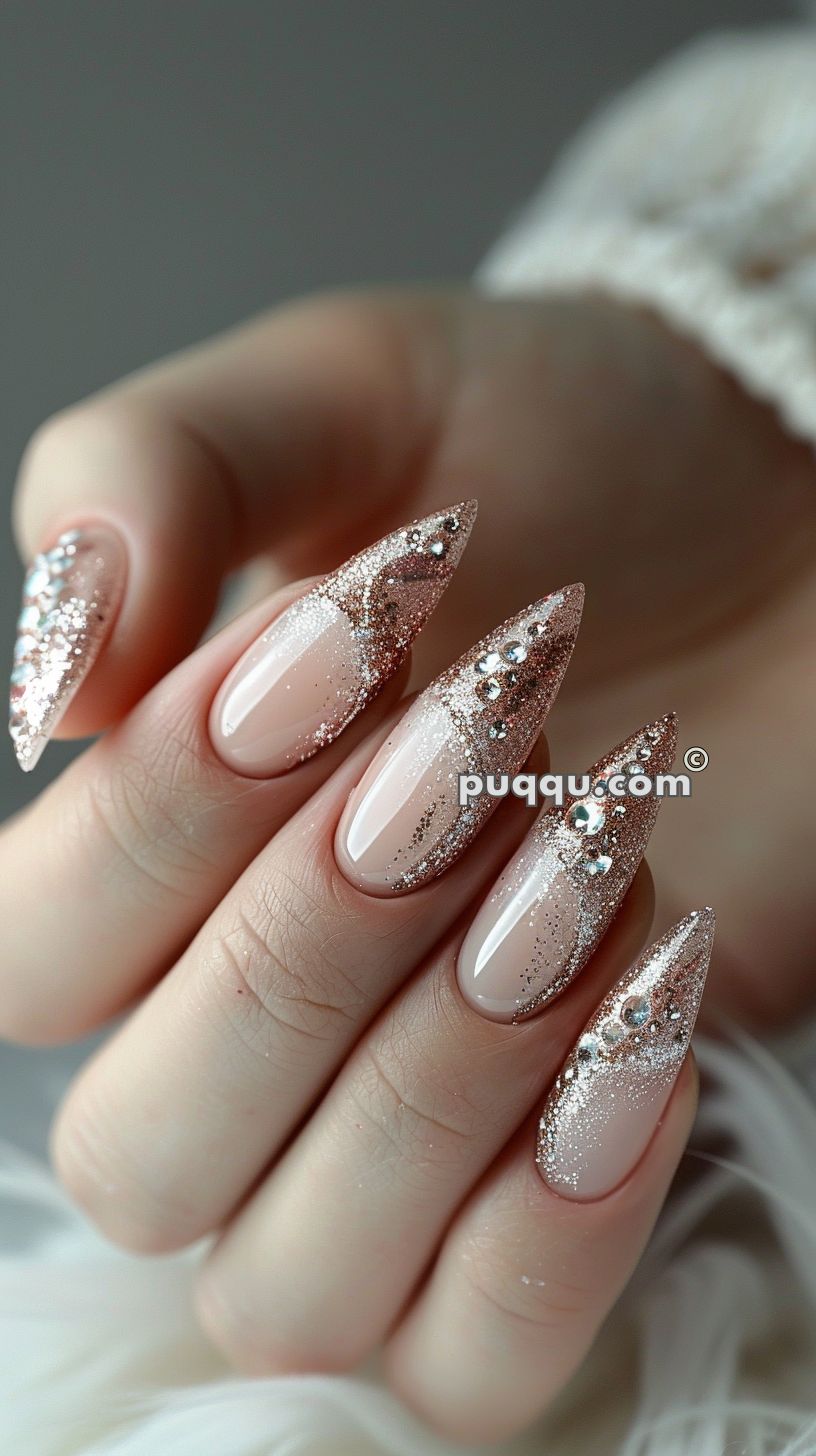 Long almond-shaped nails with a nude base, rose gold glitter tips, and rhinestone accents.