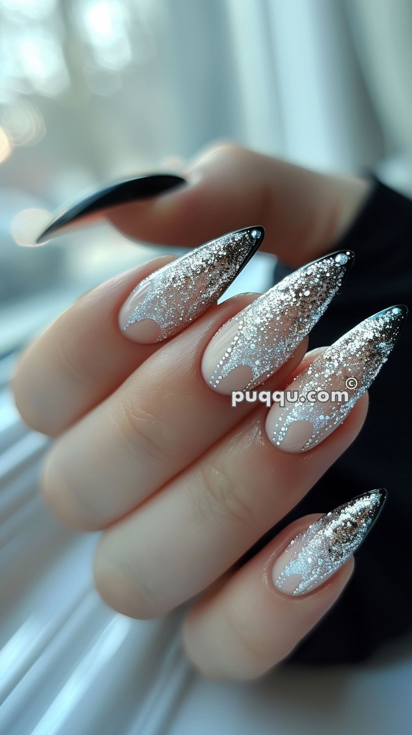 Close-up of a hand with long, pointed nails featuring a black and glitter gradient design.