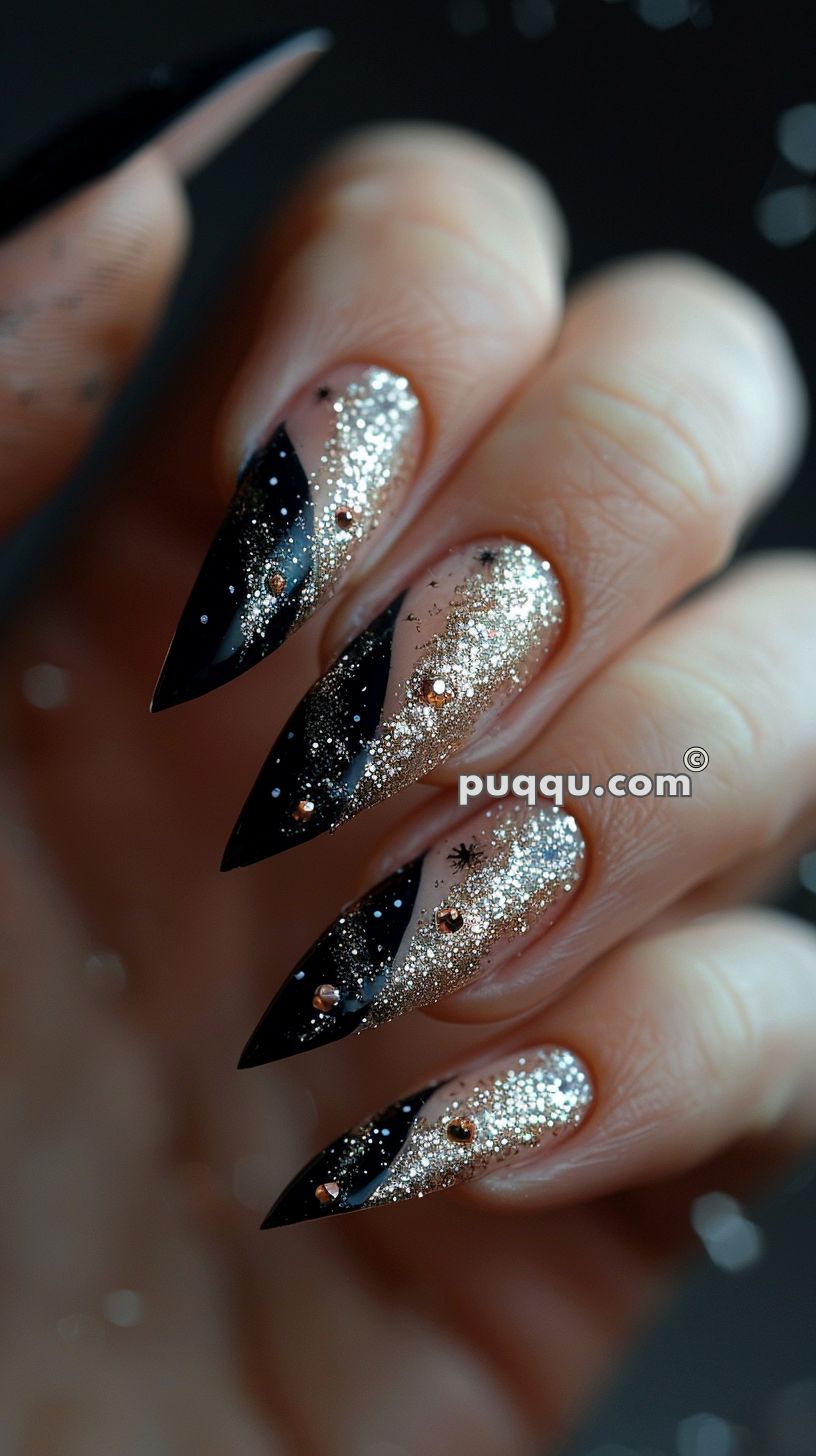 Long, stiletto-shaped nails with a black and glittery gold design adorned with small rhinestones.