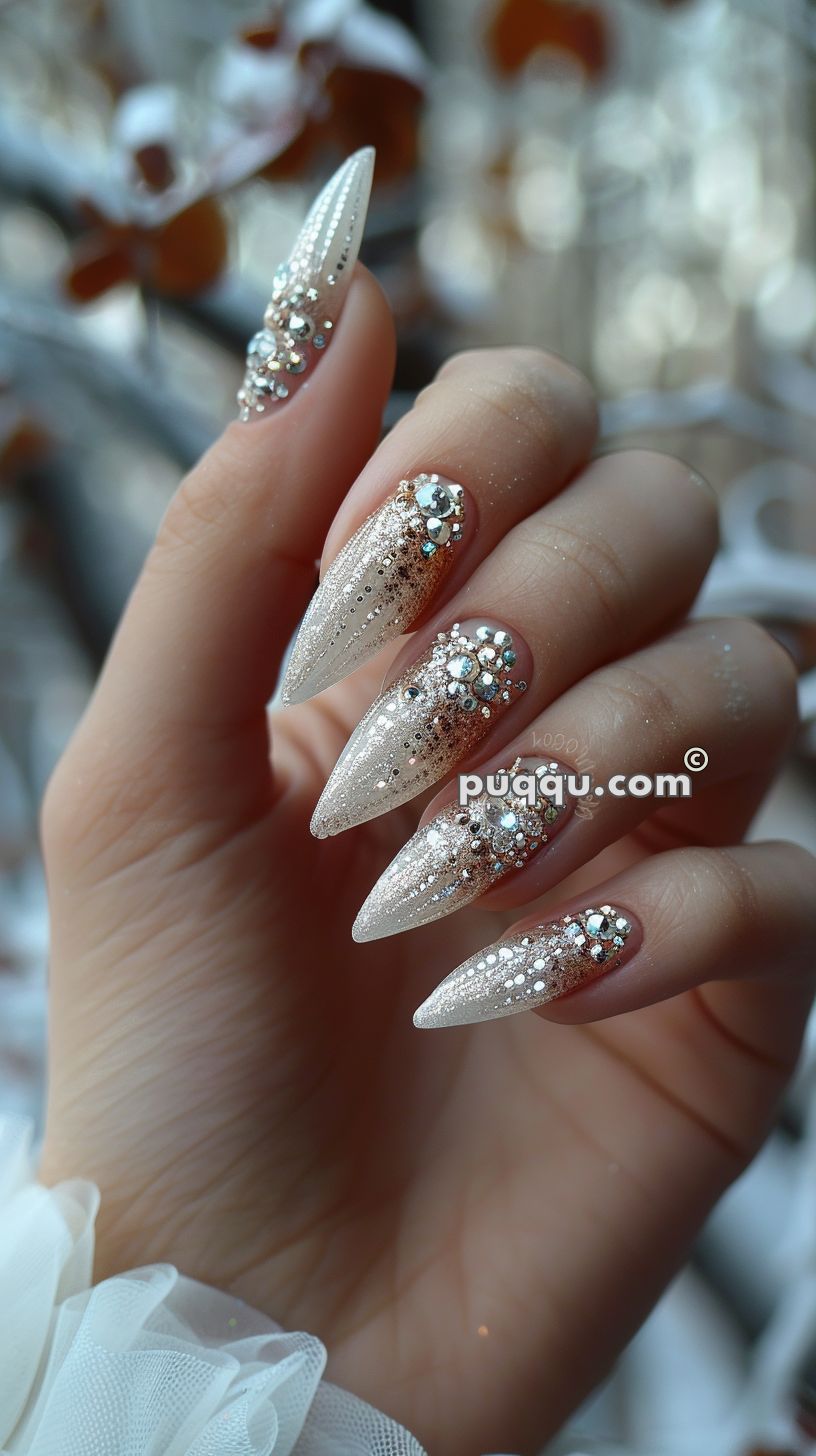 A hand with long, pointed nails featuring an intricate design with glitter and rhinestones.