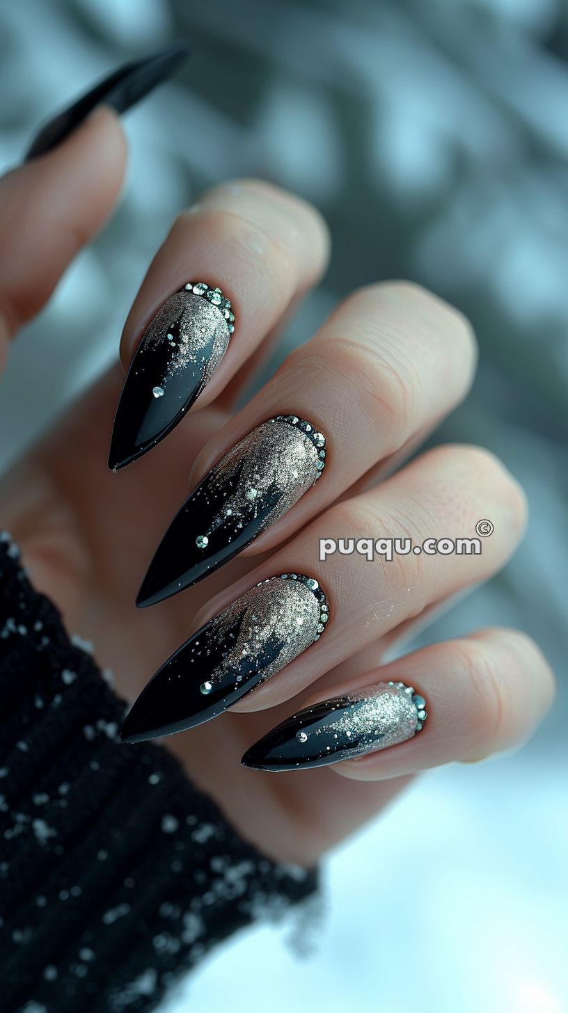 Hand with long, pointed black nails featuring silver glitter gradient and rhinestone accents.