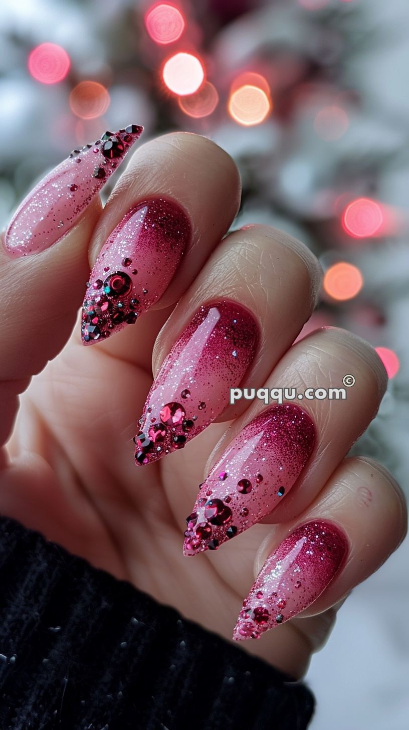Close-up of a hand with long, pointed nails decorated with red ombre glitter and adorned with red and black rhinestones.