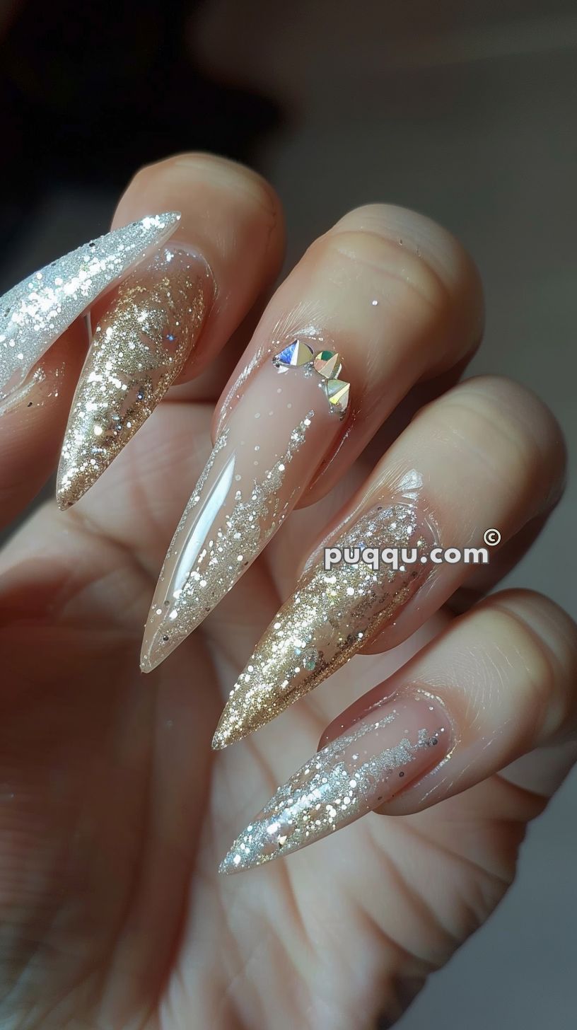 Long stiletto nails with gold glitter and rhinestone decorations.