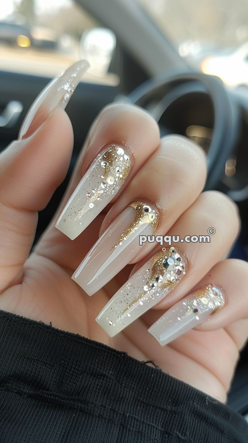Long acrylic nails with a clear base, decorated with gold glitter and rhinestones.