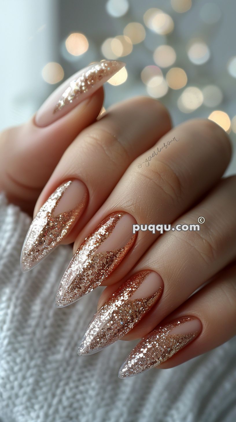 Hand with long almond-shaped nails featuring a nude base and rose gold glitter gradient tips.