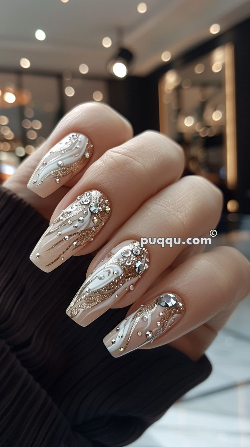 Close-up of a hand with long, intricately designed nails featuring white, gold, and silver patterns with rhinestone accents.