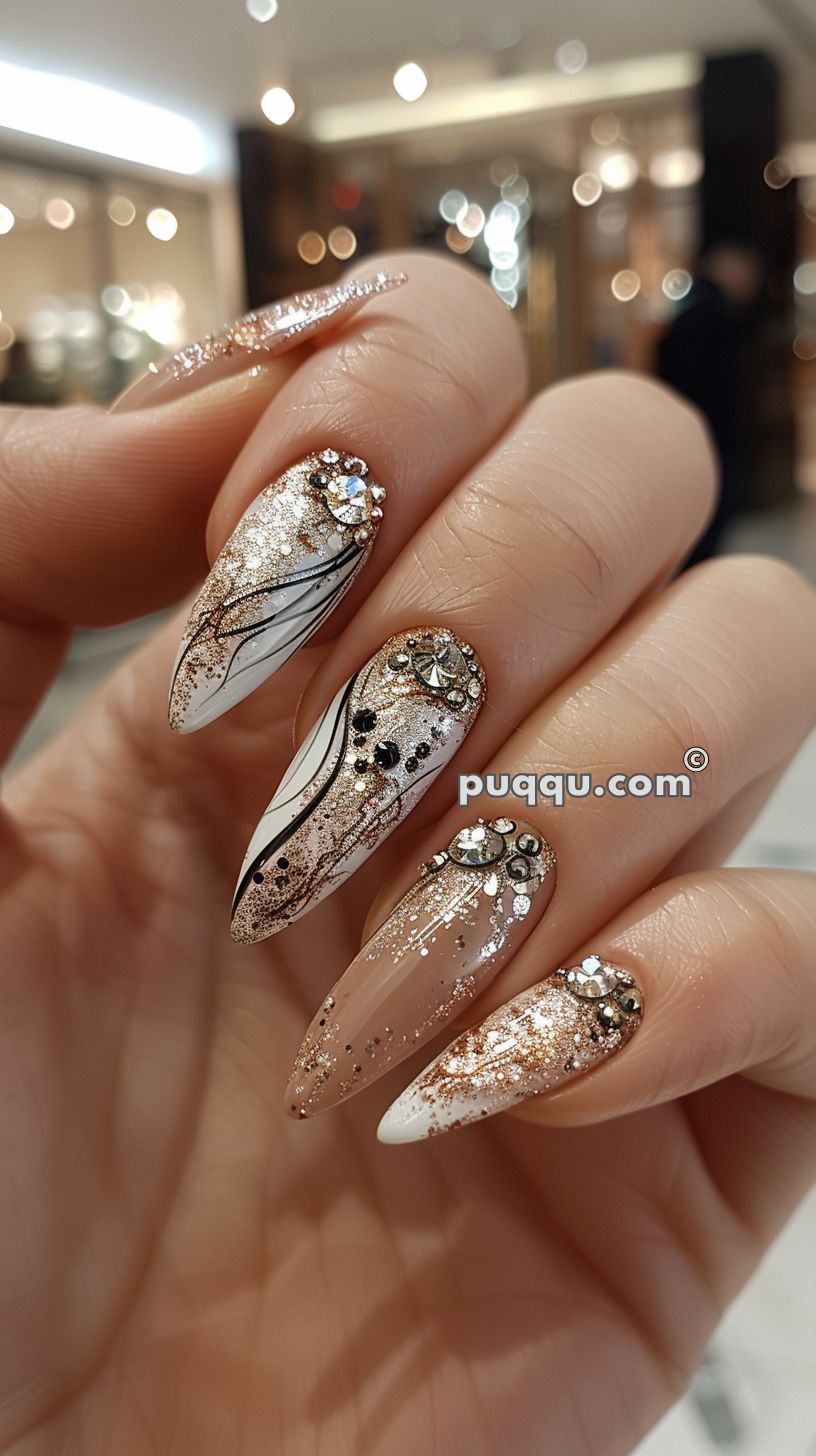 Close-up of manicured nails with a glittery, brown and gold design, adorned with rhinestones and detailed black lines.