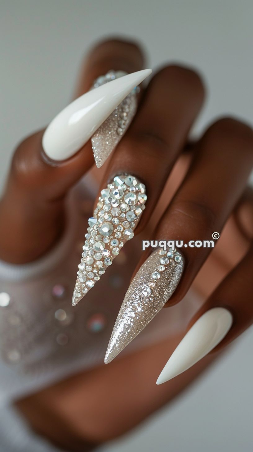 Close-up of hand with long stiletto nails painted white and accented with sparkling rhinestones and glitter.