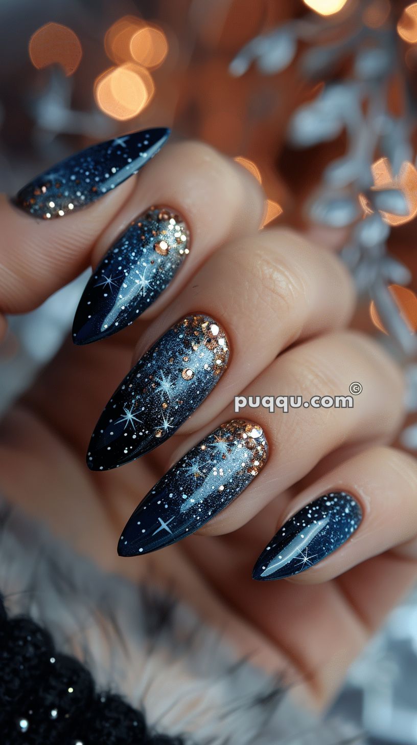 Long, almond-shaped nails with a dark blue gradient featuring a starry night sky design, embellished with gold glitter at the base and white star patterns.