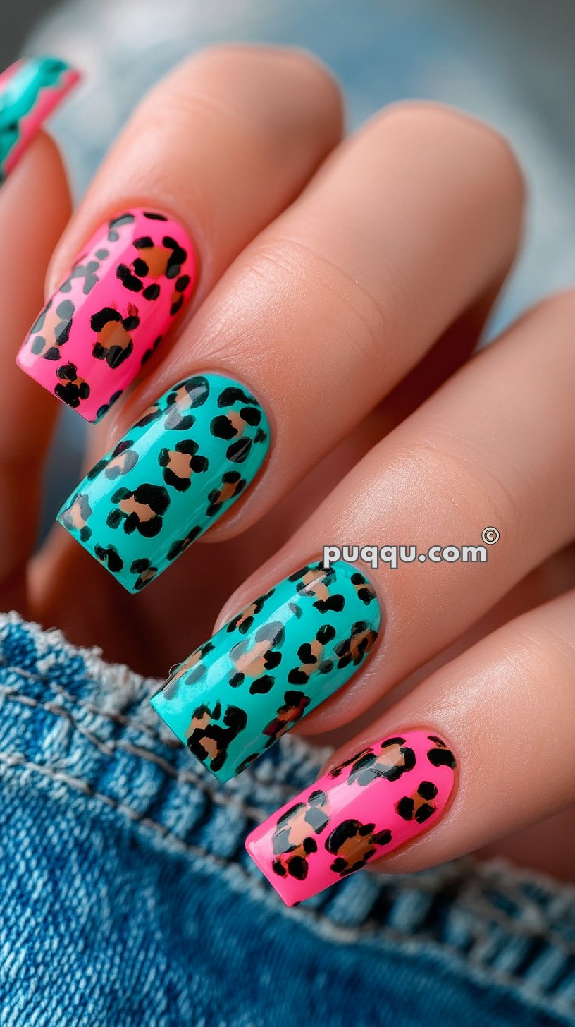 Close-up of a hand with long, square-shaped nails painted with vibrant pink and teal leopard print design.