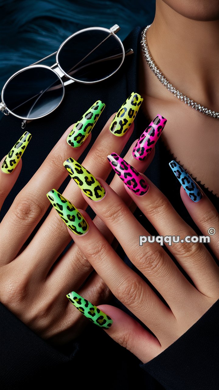 Hands showing off long, neon-colored leopard print nails in green, yellow, pink, and blue, with sunglasses and a sparkly necklace visible in the background.