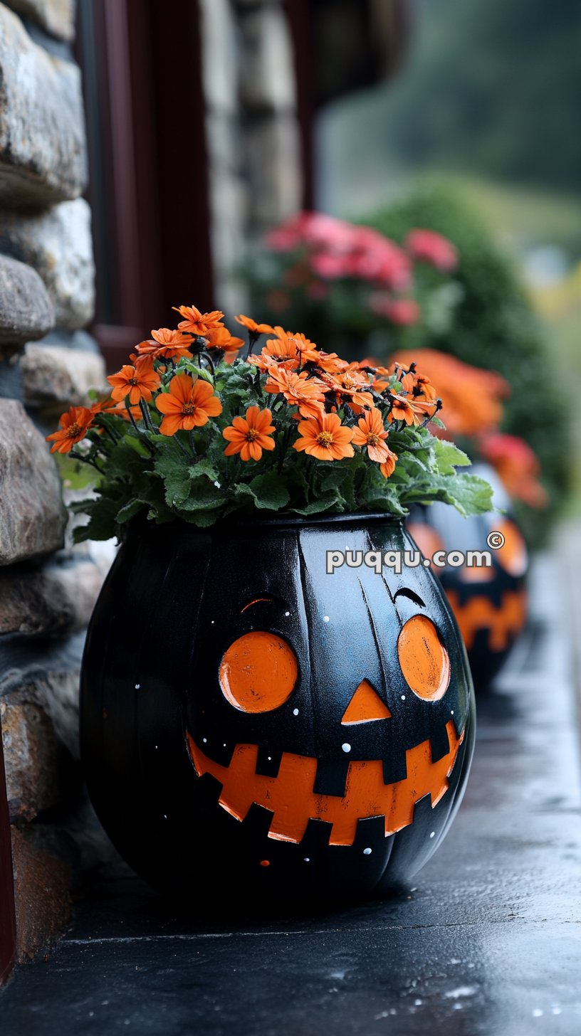 Black pumpkin-shaped flower pot with a carved jack-o'-lantern face, filled with orange flowers, placed on a stone ledge.