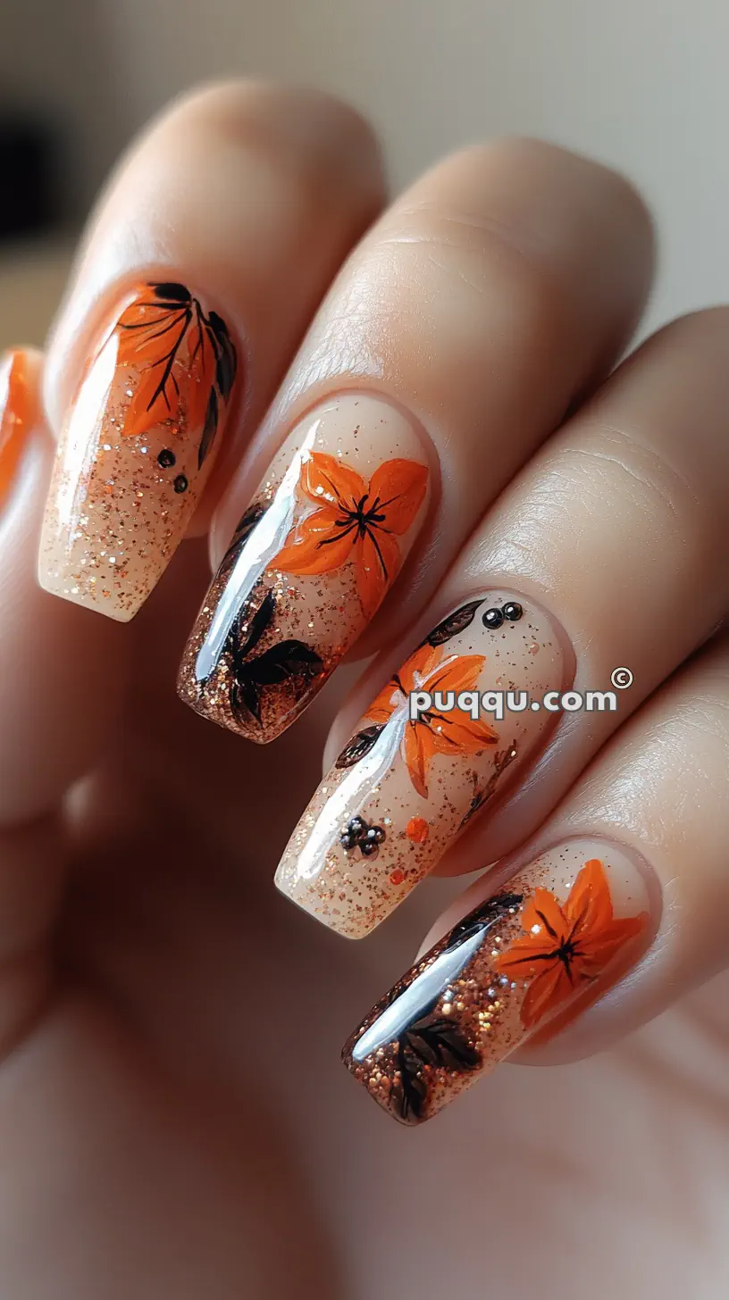 Close-up of nails with autumn-themed nail art featuring orange flowers, black leaves, and glitter accents.