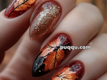 Nails with an autumn-themed design featuring intricate orange leaf patterns and gold glitter accents.