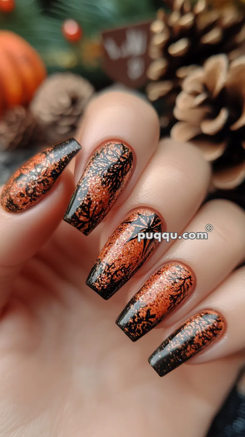 Close-up of nails with orange glitter nail polish featuring intricate black designs against a background of pine cones and blurred decorations.