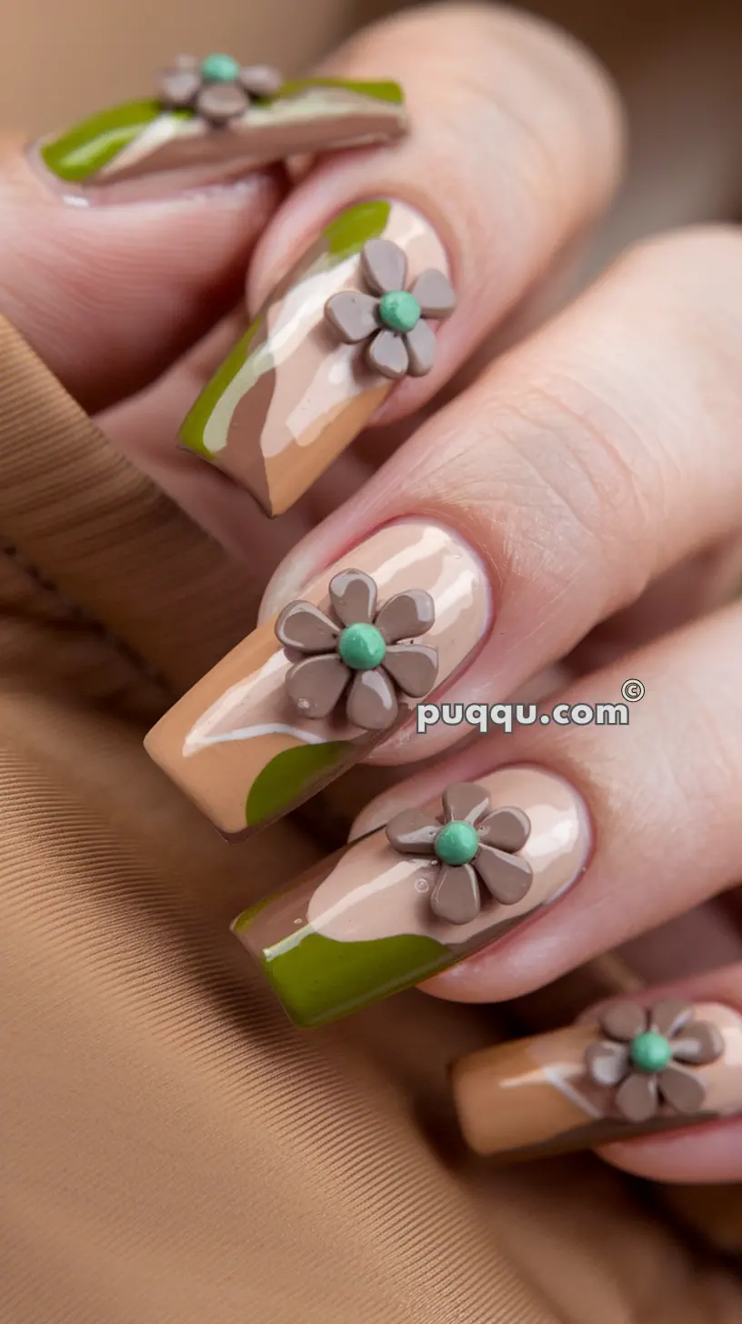 Close-up of a hand with long, rectangular nails featuring beige, green, and tan abstract design, adorned with 3D brown flowers with green centers.