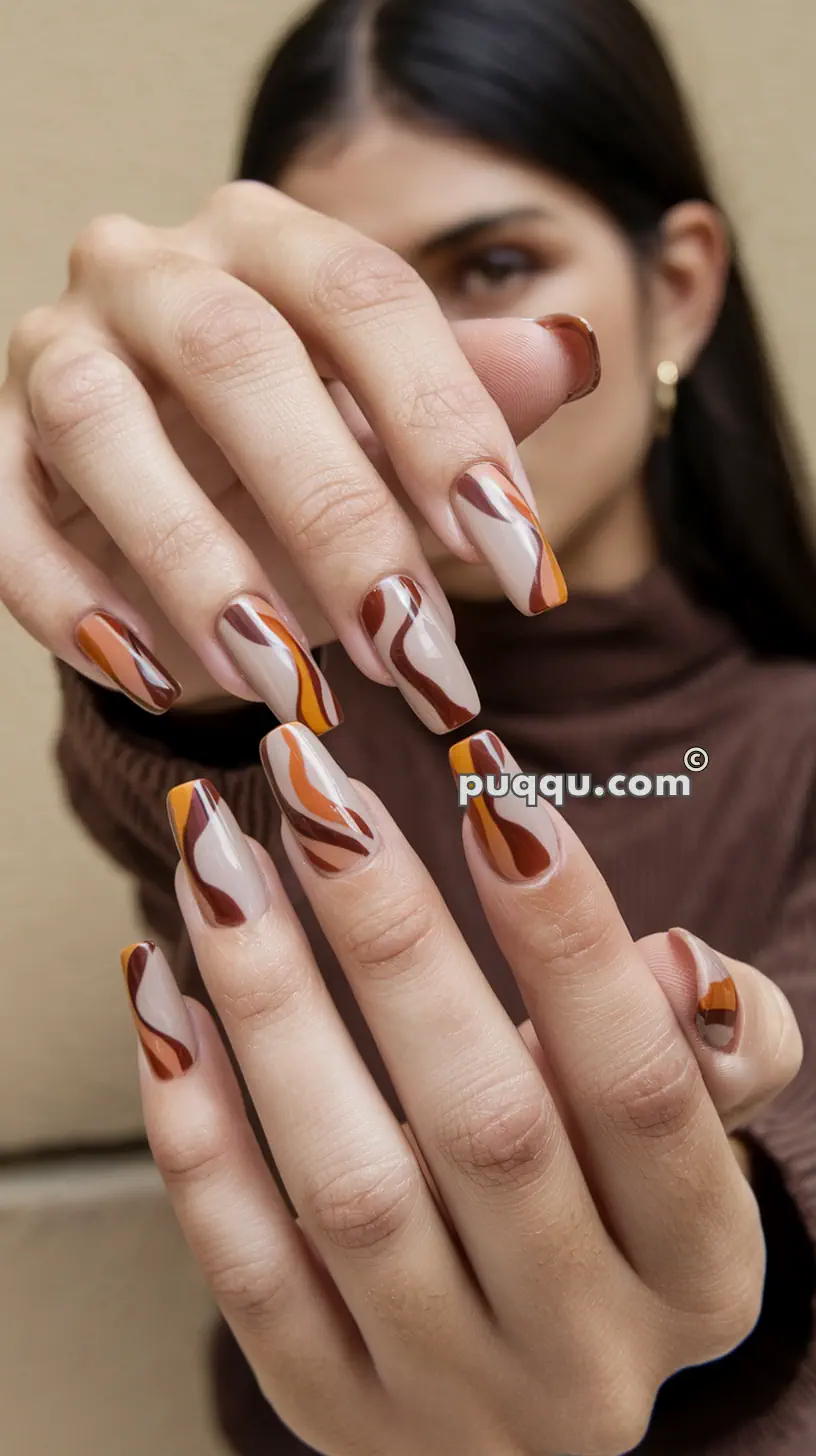 Close-up of a person with long nails featuring a marbled design in shades of brown, white, and orange.