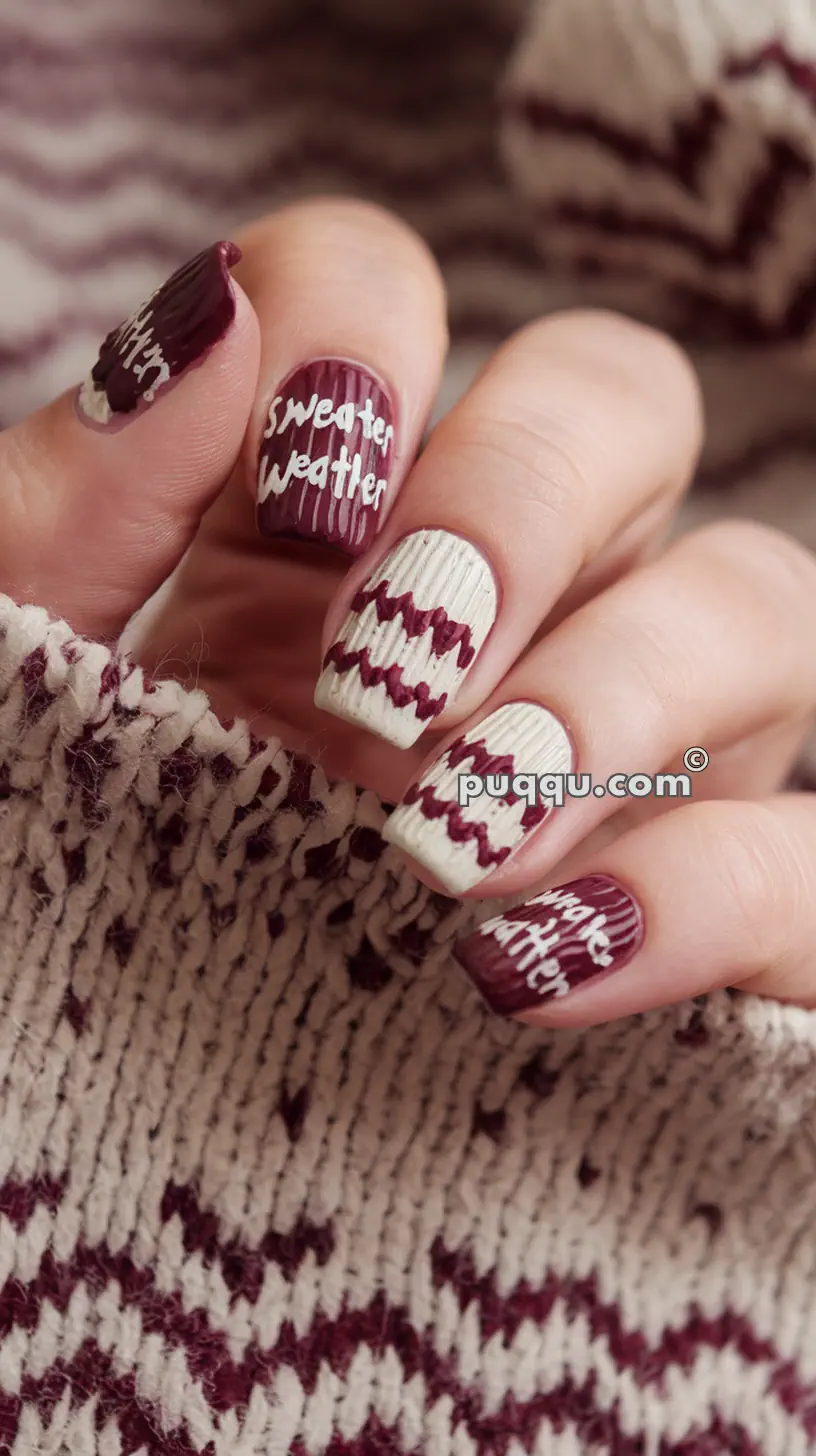 Close-up of a hand with nails painted in maroon and beige with sweater-like patterns and the text "Sweater Weather" on some nails. The background shows knit fabric in similar colors.