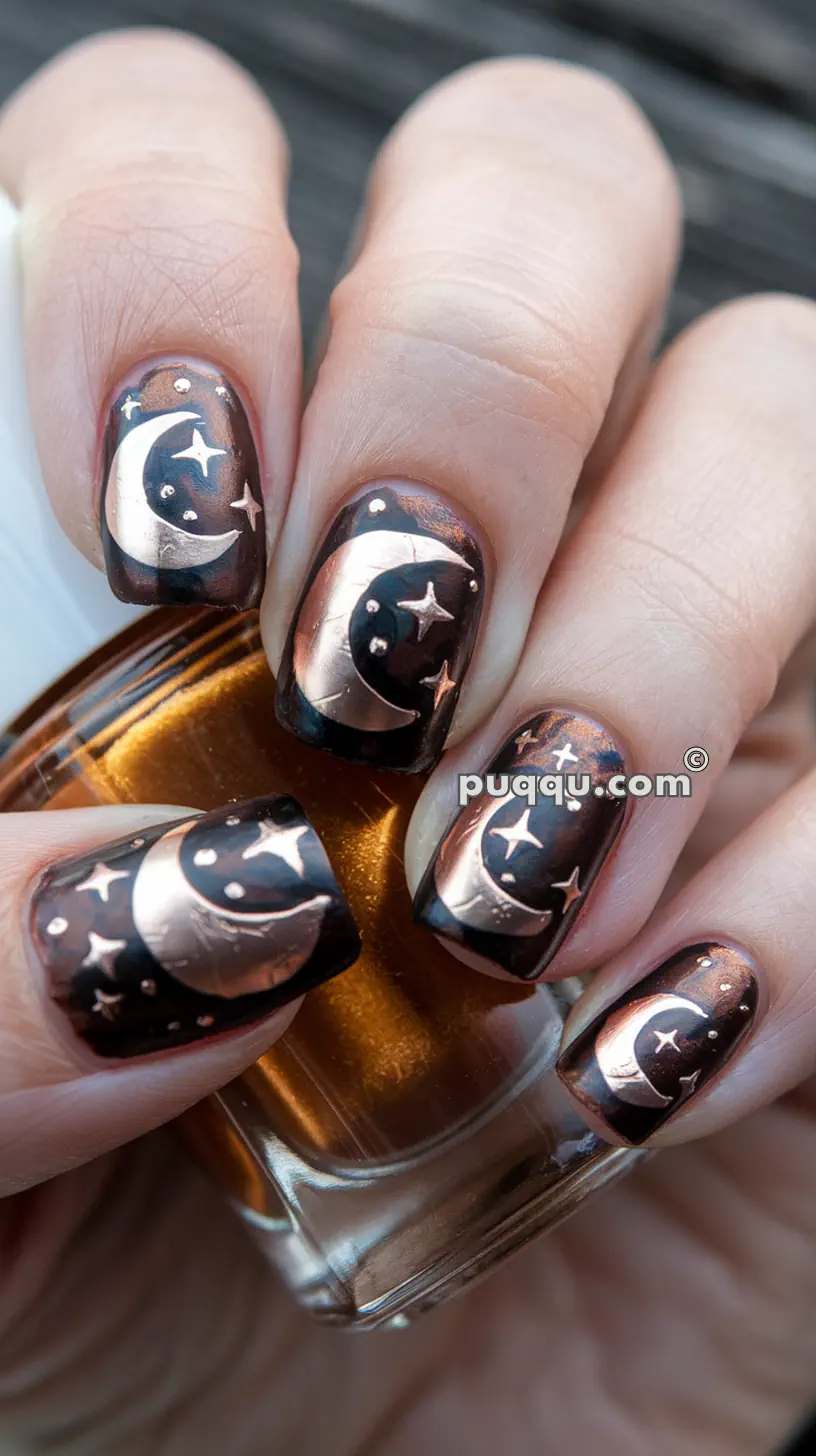 Nails painted in a dark, metallic brown polish with copper moon and star designs.