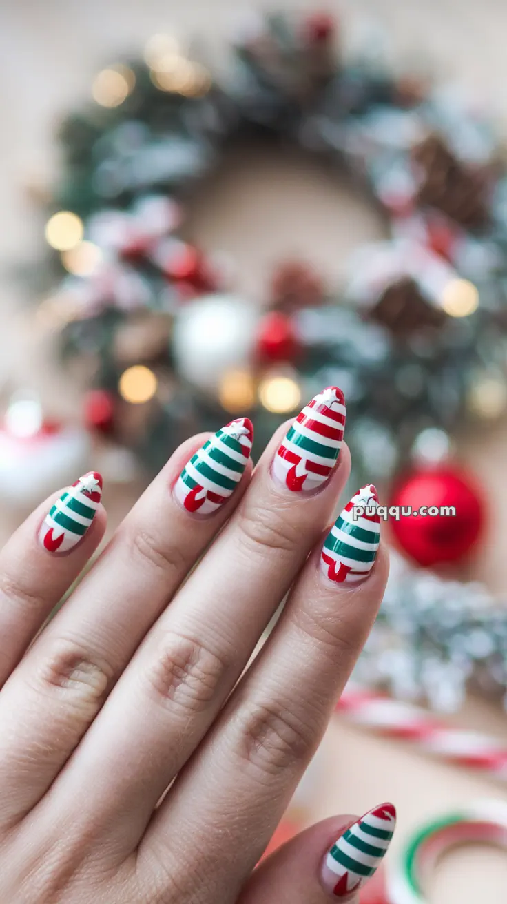 Fingers with Christmas-themed nail art featuring red and green stripes and candy cane patterns, with a blurred festive wreath in the background.