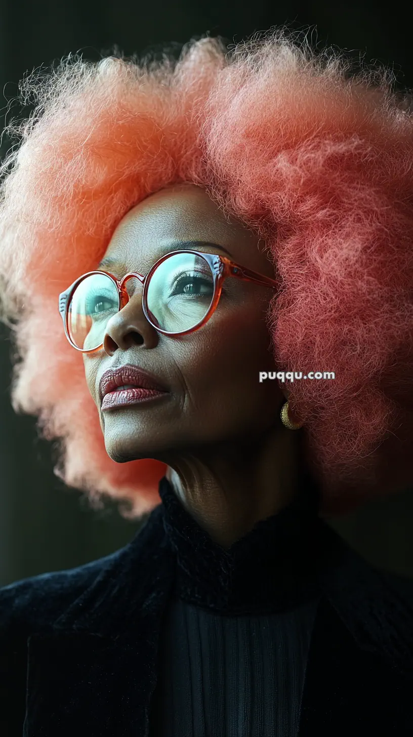 A person with large glasses and vibrant coral-colored curly hair looks upwards.