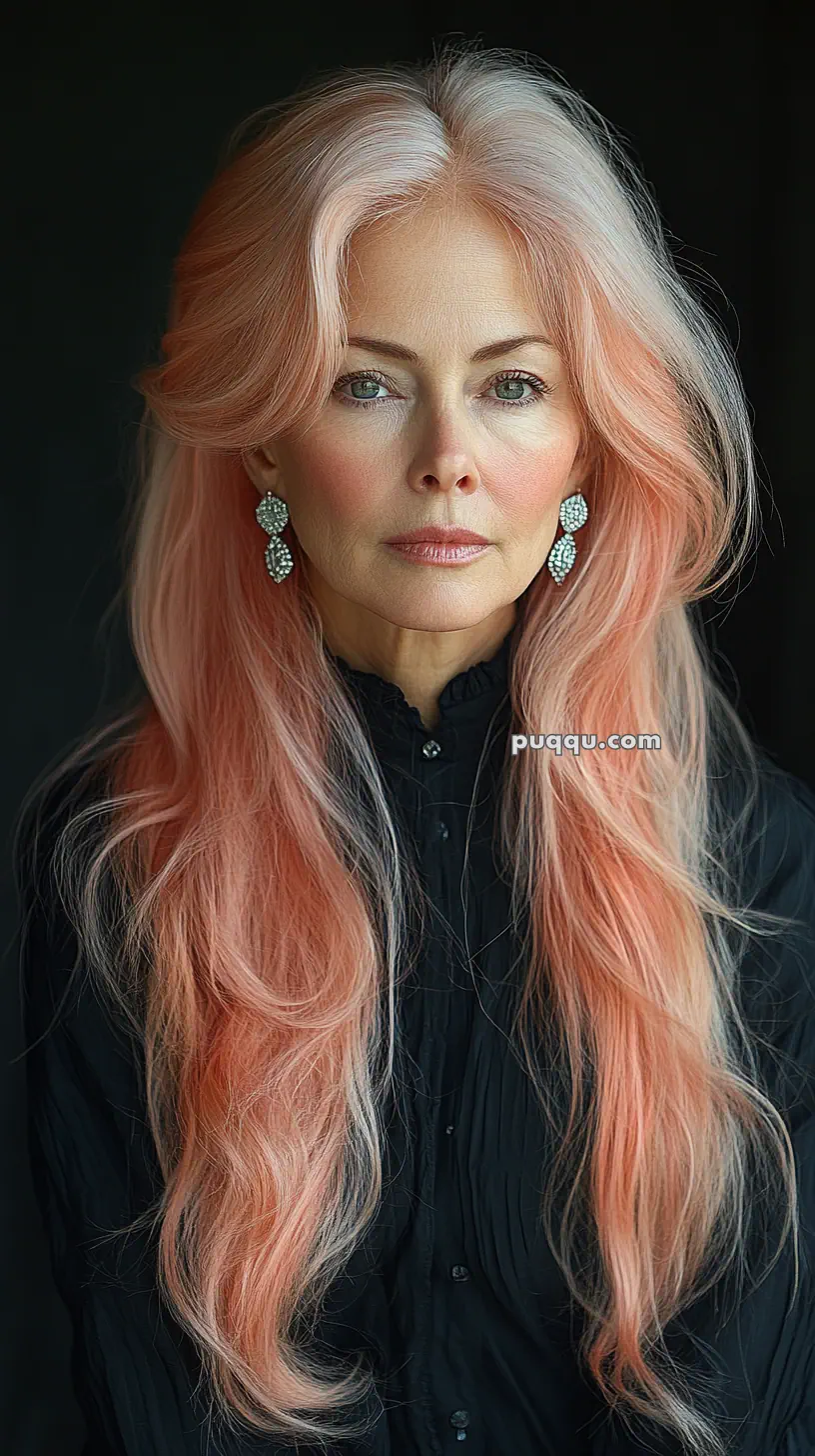 Woman with long pink hair wearing a black top and earrings.
