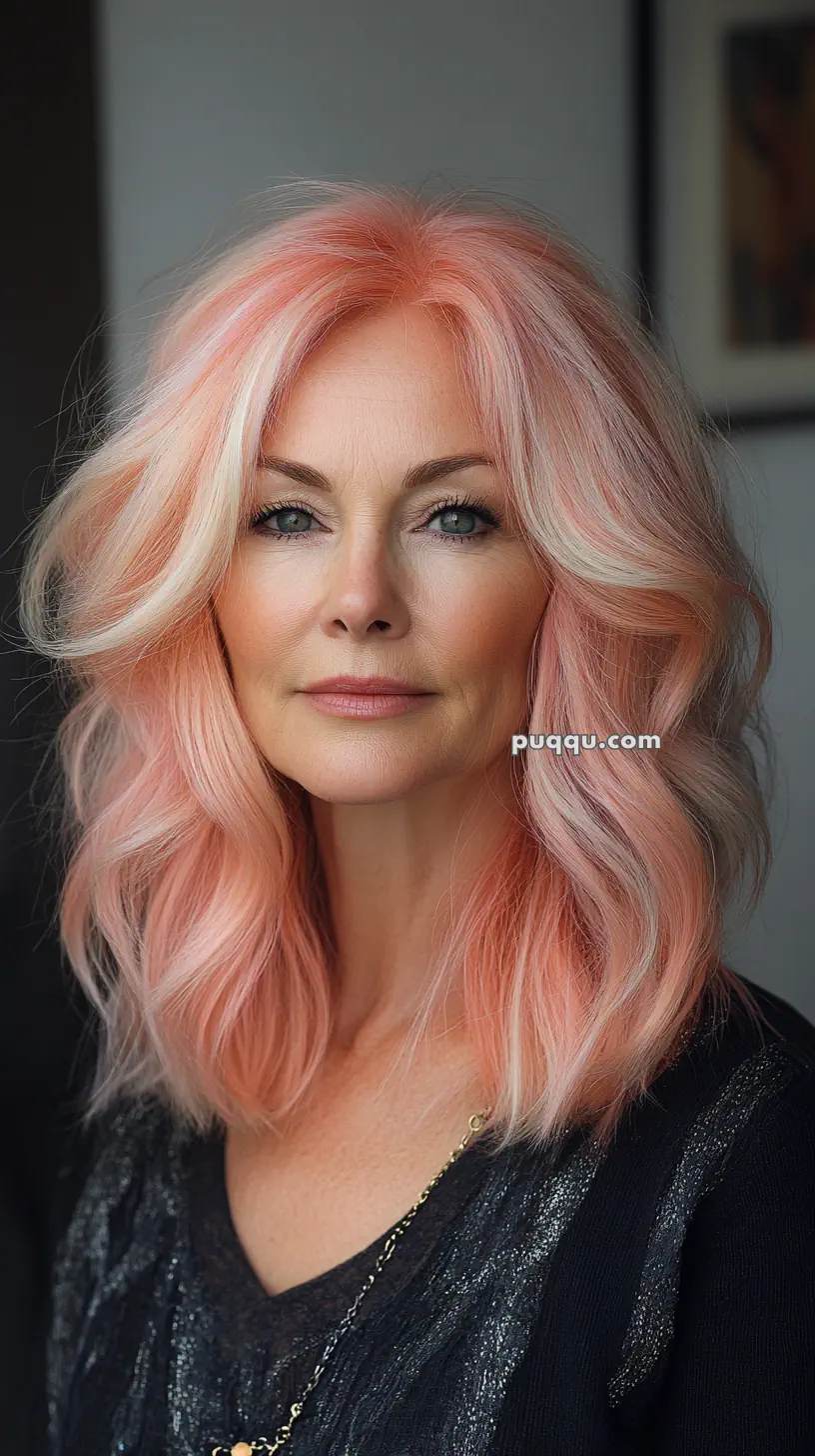 Woman with wavy pastel pink hair and subtle makeup against a dark background.