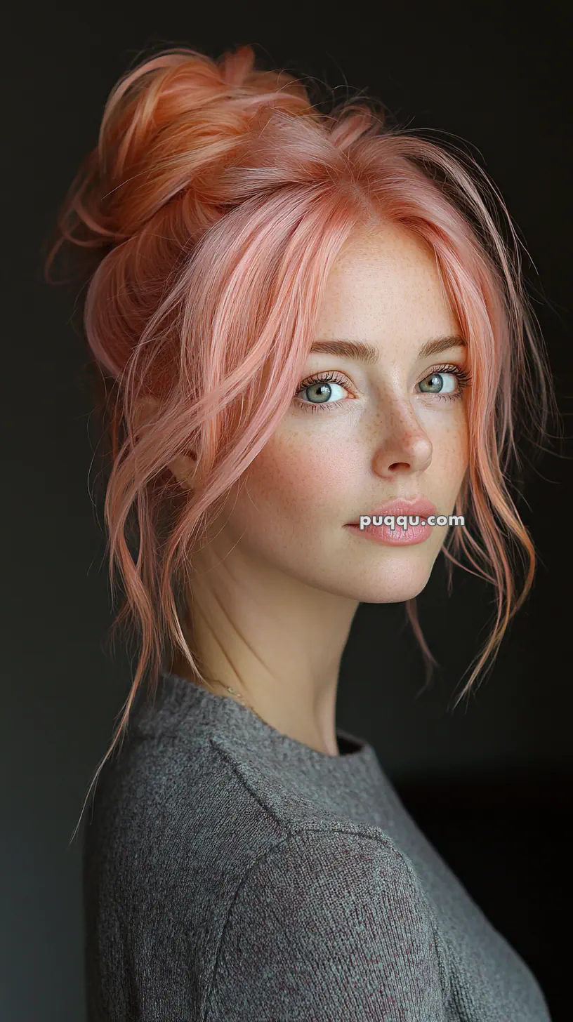 Portrait of a person with pink hair styled in a bun, wearing a grey sweater.