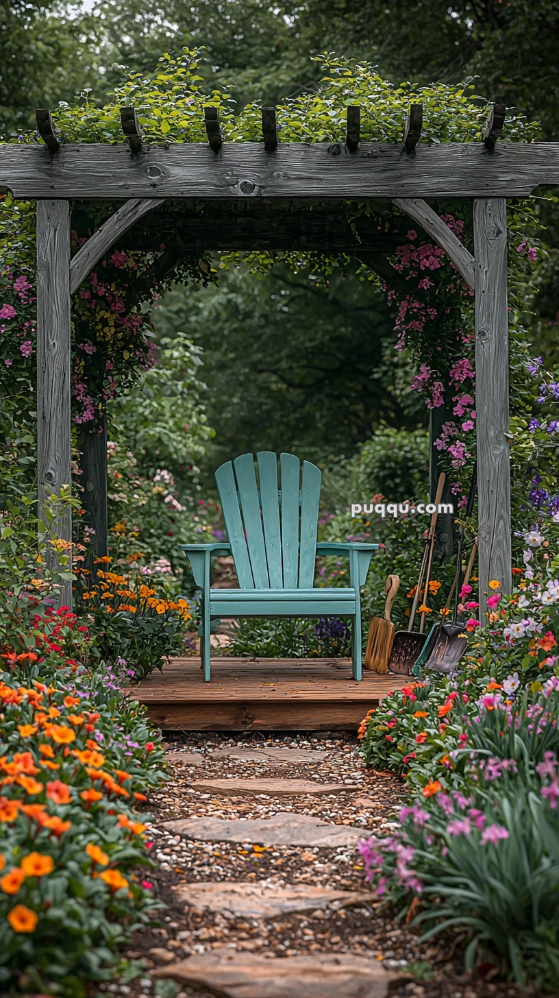 A turquoise Adirondack chair sits under a wooden pergola adorned with vibrant climbing flowers and surrounded by a lush garden with colorful blossoms. Garden tools are propped on the right side beside the chair.