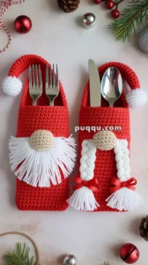 Two crocheted utensil holders designed like gnomes, with one featuring a white beard and the other with white braided hair, each holding forks and spoons. The holders are surrounded by Christmas decorations including pine cones, bells, and greenery.